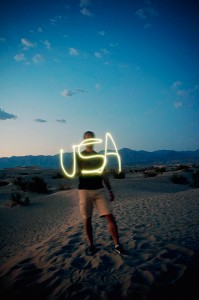 David est debout dans le sable de Mesquite Dunes dans la Vallée de la Mort (Death Valley) et il écrit le mot USA avec un briquet (appareil photo en pose longue) au coucher du soleil